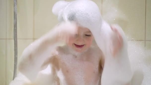 Забавна дитина грає з водою і піною у ванній — стокове відео