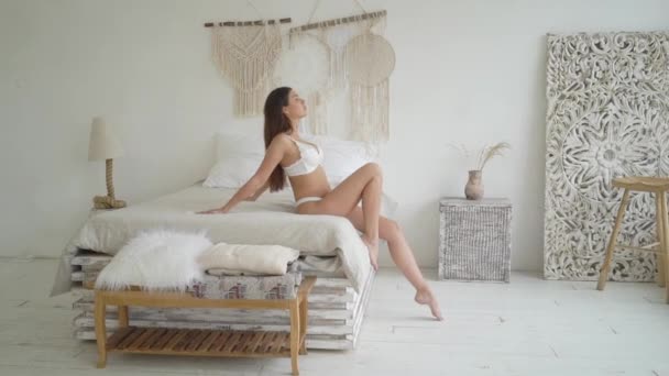 Szexi barna hölgy pózol a fehér fehérnemű, ül az ágyban — Stock videók