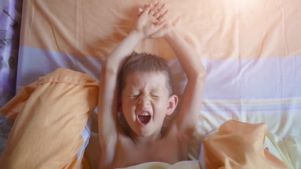 침대에서 팔을 스트레칭하는 동안 하품 하는 어린 소년의 상단 보기 — 비디오