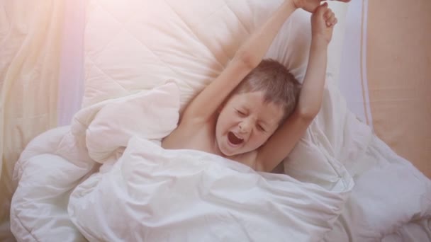 Blick von oben auf einen kleinen Jungen, der gähnt und sich im Bett dehnt — Stockvideo