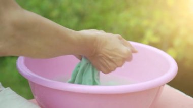 Yaşlı kadın pembe plastik bir havzada çamaşır yıkama elleri