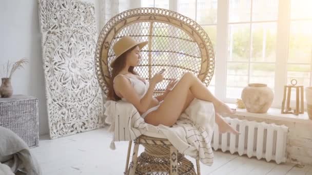 Shopping online. Sexy woman in straw hat sitting in cozy armchair and holding bank card while shopping online via tablet — Stock Video
