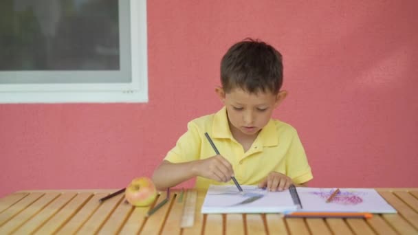 Netter kleiner Junge zeichnet in seinem Album auf Holztisch — Stockvideo