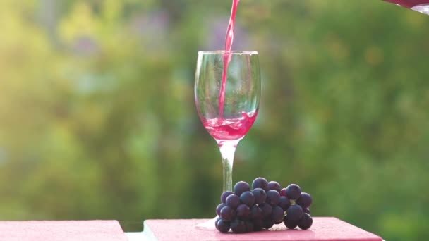 Домашнее вино наливается в бокал на зеленом фоне природы — стоковое видео