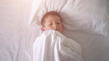 Yatakta esneyen ve esneyen genç bir çocuğun üst görünümü