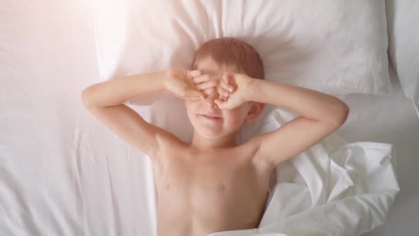 Vue du dessus d'un jeune garçon bâillant au lit — Video