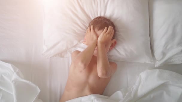 Vue du dessus d'un jeune garçon bâillant et s'étirant au lit — Video