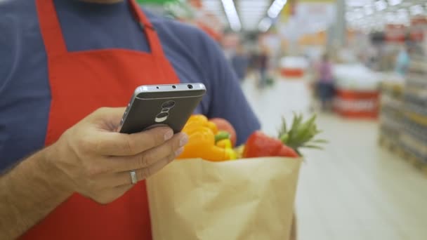 超级市场员工使用手机并在超级市场拿着购物袋 — 图库视频影像
