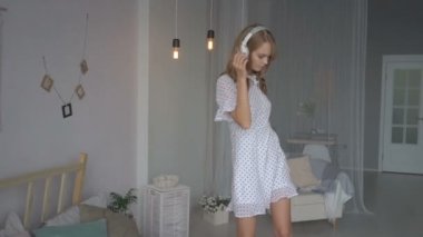 Kulaklıklı mutlu genç bir kadın akıllı telefondan müzik dinliyor ve evde yatakta dans ediyor.