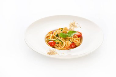 Beyaz arka planda karidesli spagetti, kiraz domatesleri, kabak ve fesleğen.