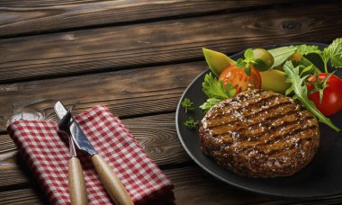 Kızarmış sığır burger pirzolası, salata ve siyah tabakta ahşap bir tabakta otlar.
