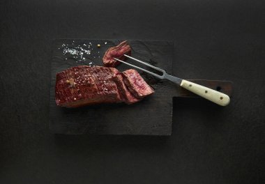 Orta boy biftek, ahşap tahtada çatal ve tuzla dilimler.