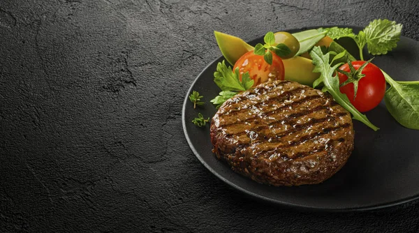 Sulu ızgara burger pirzolası ve arka planda salata yaprakları.