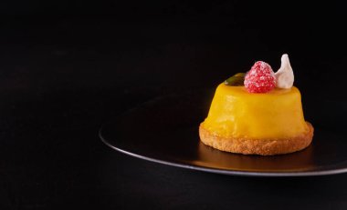 Siyah tabakta sarı jöleli mango kremalı tatlı.