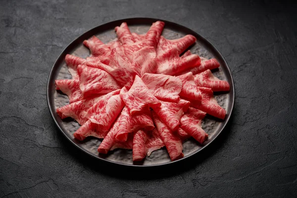 Carne de kobe japonesa cortada en rodajas en un plato preparado para shabu shabu sobre fondo negro — Foto de Stock