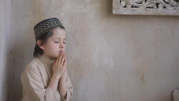 Очаровательный маленький ребенок в молитвенной шляпе и арабской одежде, молящийся Аллаху, пророку Мухаммеду святой дух религиозный символ концепции внутри восточного интерьера — стоковое видео