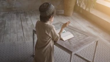 Müslüman küçük çocuk Kur 'an' ı ibadet şapkası ve Arapça giysiler içinde tespih boncukları ve Kur 'an-ı Kerim-i Kerim-i Kerim-i Kerim-i Kerim-i Kerim, Allah' a dua ederek okudu.