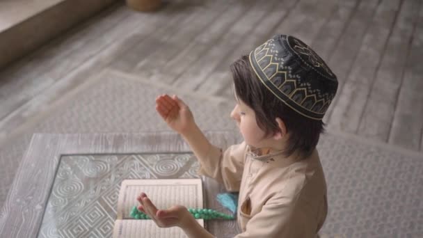 Adorabile bambino musulmano leggere il Corano in cappello di preghiera e abiti arabi con rosari e corano libro pregare Allah, profeta Muhammad Spirito Santo religione simbolo concetto all'interno dell'interno orientale — Video Stock