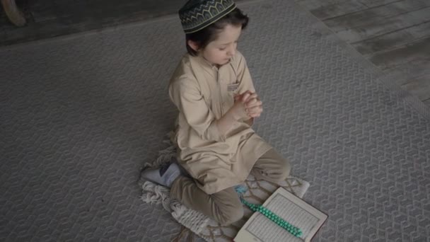 Adorable niño musulmán leer el Corán en sombrero de oración y ropa árabe con cuentas de rosario y libro del Corán orando a Allah, profeta Muhammad espíritu santo religión símbolo concepto interior oriental — Vídeo de stock