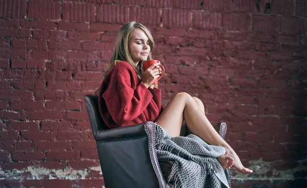 Elinde kırmızı bir fincan kahve ya da çay tutan sıcak içecek içen genç bir kadın çatı katında rahat bir sandalyede oturuyor. Mutlu, sağlıklı bir kadın sabah içkisiyle ellerde rahatlıyor. Huzurun tadını çıkarıyor..