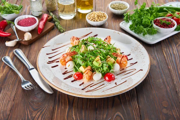 Fresh healthy avocado and shrimps salad with arugula, tomatos and mozzarella cheese on wooden background, cooking concept with ingredients — Stock Photo, Image
