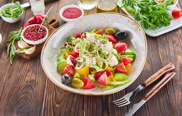 Zdravý veganský salát z čerstvé zeleniny - rajčata, avokádo, rukola, olivy a kluzká cibule na míse s přísadami na dřevěných kulisácích. Dietní jídlo vaření koncept — Stock fotografie