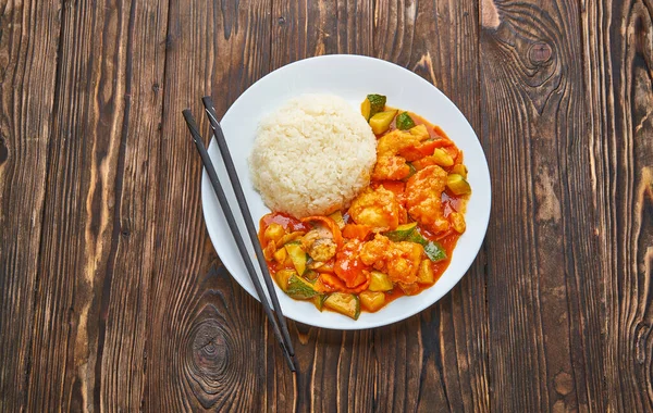 Frango doce e azedo em molho de laranja com legumes, arroz e pauzinhos em fundo de madeira, conceito de comida asiática vista superior com espaço de cópia — Fotografia de Stock