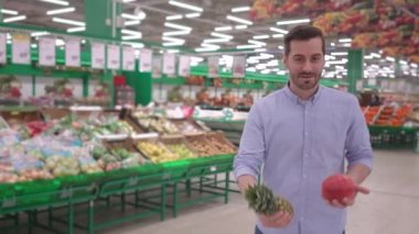 Çekici genç adam marketteki raflarda organik sebzelerle dans ediyor. Gülümsüyor ve gülüyor.