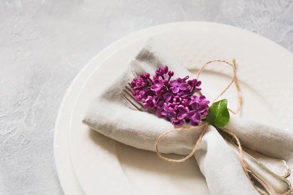 Spring elegant table place setting with violet lilac, silverware on vintage table. View from above.