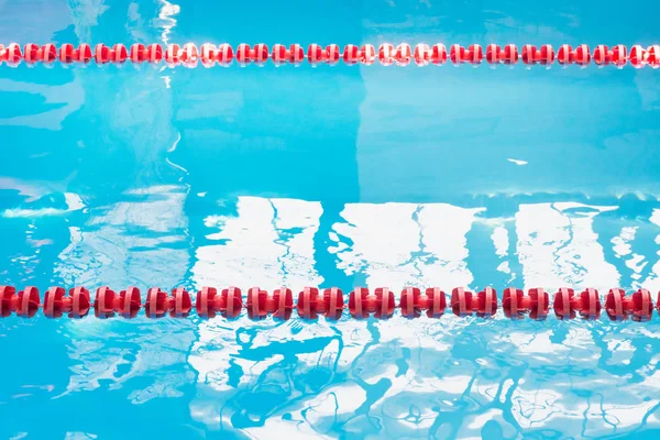 Blue pool water and red swimming lane marker in swimming pool with sun reflections. Abstract blurred pattern.