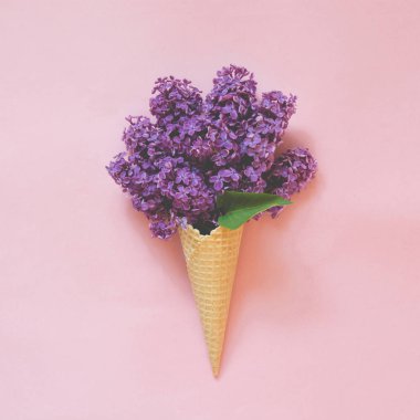 Yaratıcı natürmort. Dondurma koni soluk pembe bir arka plan üzerinde Mor Lila çiçek buketi. Bahar kavramı. Yukarıdan görüntülemek.