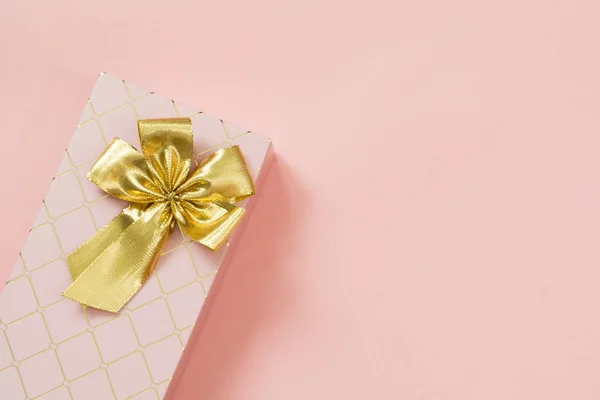 Female gift box with golden ribbon on punchy pastel pink. Birthday. Copy space. Top view.