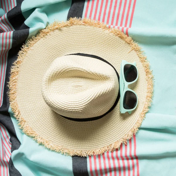 Straw beach sun-hat and sun glasses on pastel pink and mint pareo. Female outfit for beach. Summer concept. Close up.