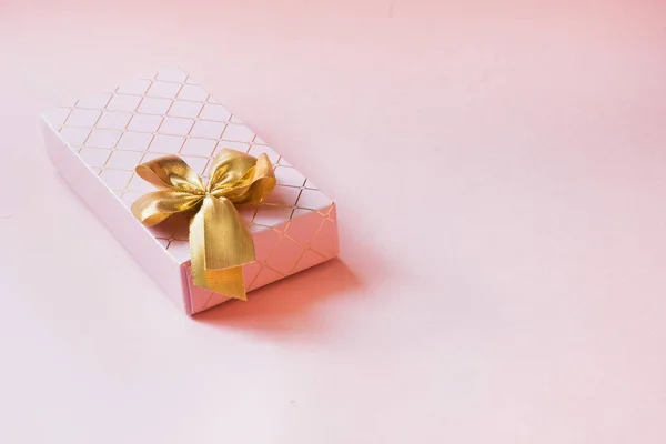 Female gift box with golden ribbon on punchy pastel pink. Birthday. Copy space. Top view.