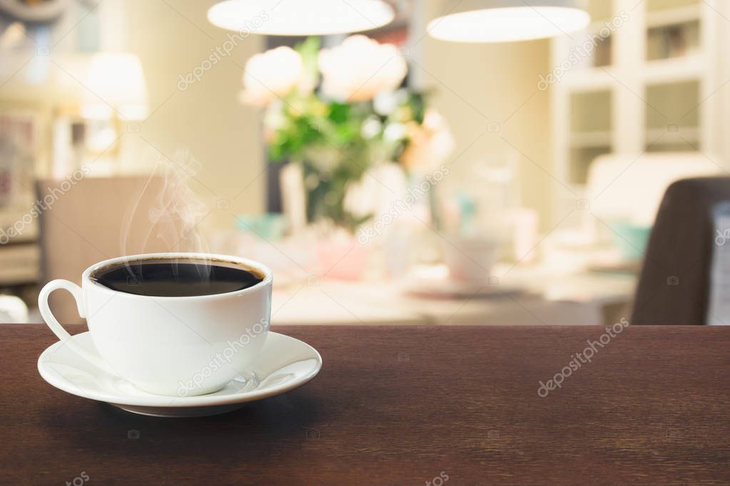 Cup of black coffee on wooden tabletop in blurred modern kitchen or cafe. Close up. Indoors.