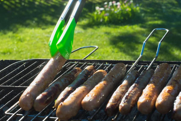 Tasty sausages grilling on portable barbecue on summer picnic. Outdoors. Smoke and fire. Close up.