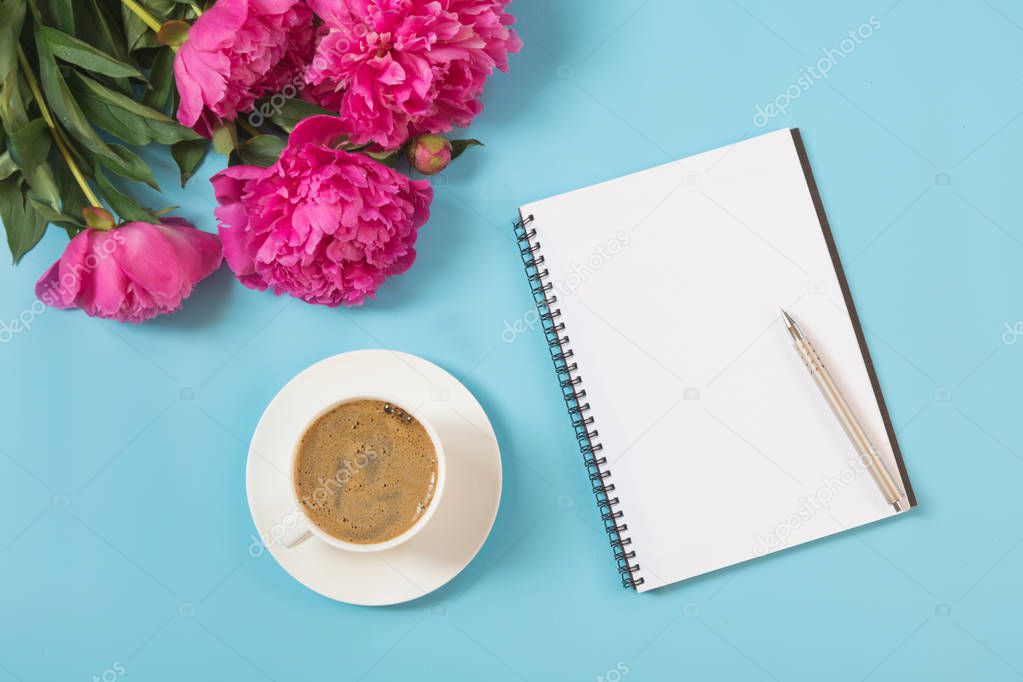 Bouquet of pink peony flower and white copybook with pen on punchy pastel blue. Working desk. Copy space. Top view. Flat lay. Female accessories for target planning.