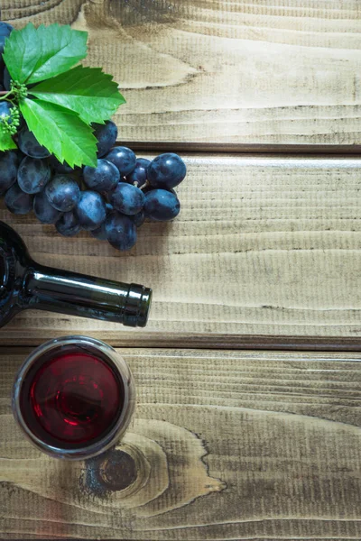 Açık bir şişe kırmızı şarap cam, tirbuşon ve ahşap arka plan üzerinde olgun üzüm ile. Kopya alanı ve üstten görünüm.