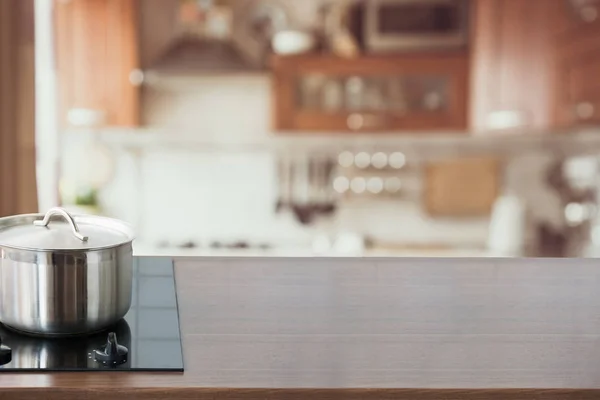 Blurred and abstract kitchen background. Wooden tabletop with pan and defocused modern kitchen for display your products.