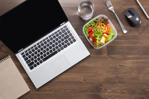 Healthy business lunch in office, salad, water on wooden table. Top view with copy space. Concept healthy nutrition. Lunchbox.