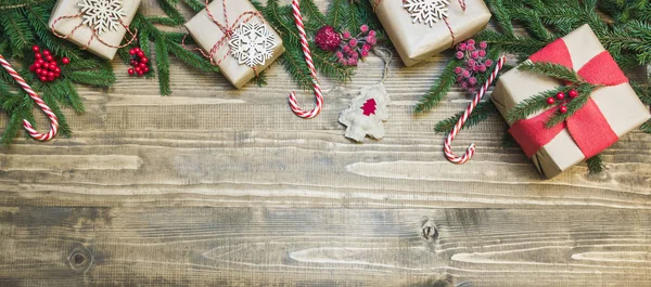 Christmas holiday banner - gifts, holly berries and decoration on wooden board. Holiday card. Top view.