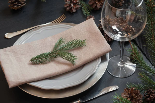 Christmas table setting with silverware and dark natural evergreen decor on black table. Close up. Holiday Centerpieces.