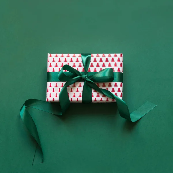 Christmas giftbox with green ribbon on green surface. Xmas card. Top view.