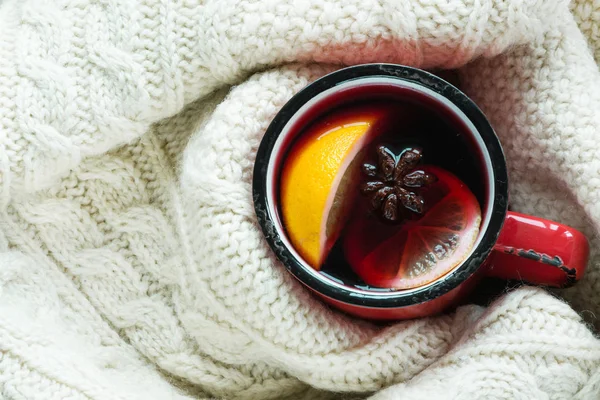 Christmas traditional hot beverage. Mulled wine in red mug with spice wrapped in warm green scandinavian sweater.