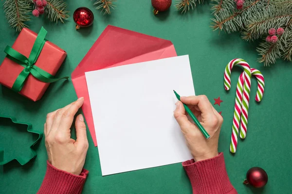 Kerst lege lege brief aan Santa of uw verlanglijst of komst activiteiten op groen. Vrouwelijke hand schrijven. Bovenaanzicht. — Stockfoto