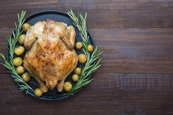 Roast Chicken with potatoes and Rosemary on Wooden Table. Copy space.