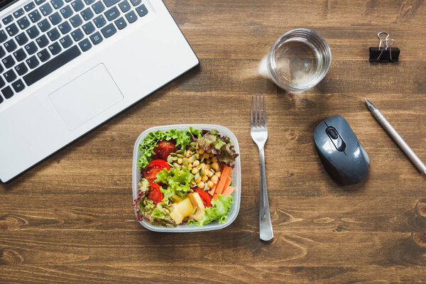 Healthy business lunch in office, salad, water on wooden table. Concept healthy nutrition. Lunchbox.