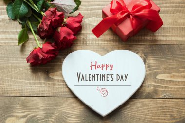 Sevgililer günü tebrik kartı buket kırmızı gül çiçek, kalp boş olarak ve hediye kutusu ahşap masa üzerinde. Üstten görünüm.