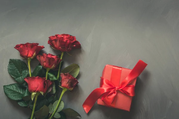 Cartão dos namorados com espaço de cópia. Buquê de rosas vermelhas e presente romântico na placa cinza . — Fotografia de Stock