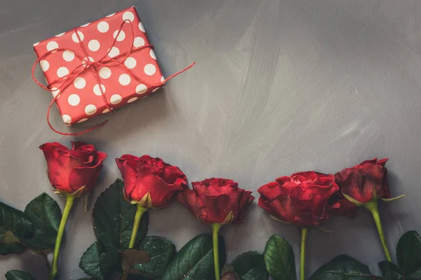 Cartão dos namorados. Buquê de rosas vermelhas e presente romântico na placa cinza . — Fotografia de Stock